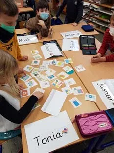 Grundschulkinder sortieren an zusammengeschobenen Tischen Bildkarten, vor ihnen liegen selbst beschriftete Namensschilder.